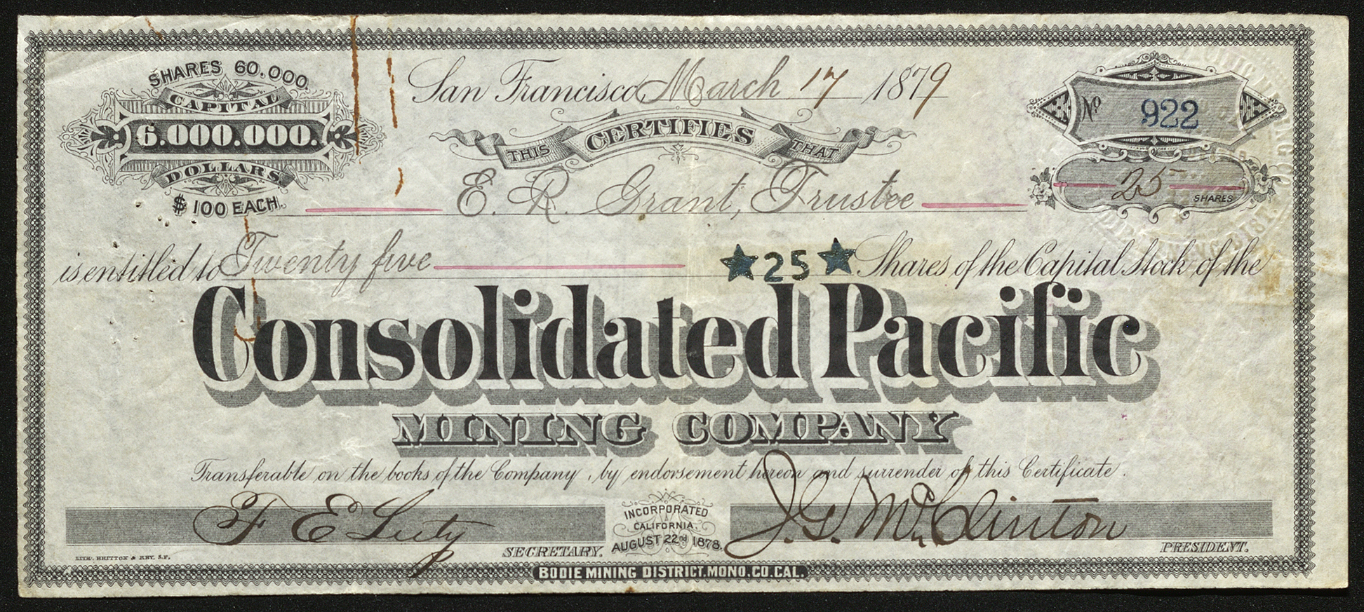 Certificate with black ink shows intricate lettering, signatures, a company seal, and a rust-colored paper clip shape stain