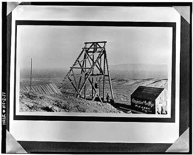 A black and white photograph with the mine hoisting works in the foreground and a small shack.
