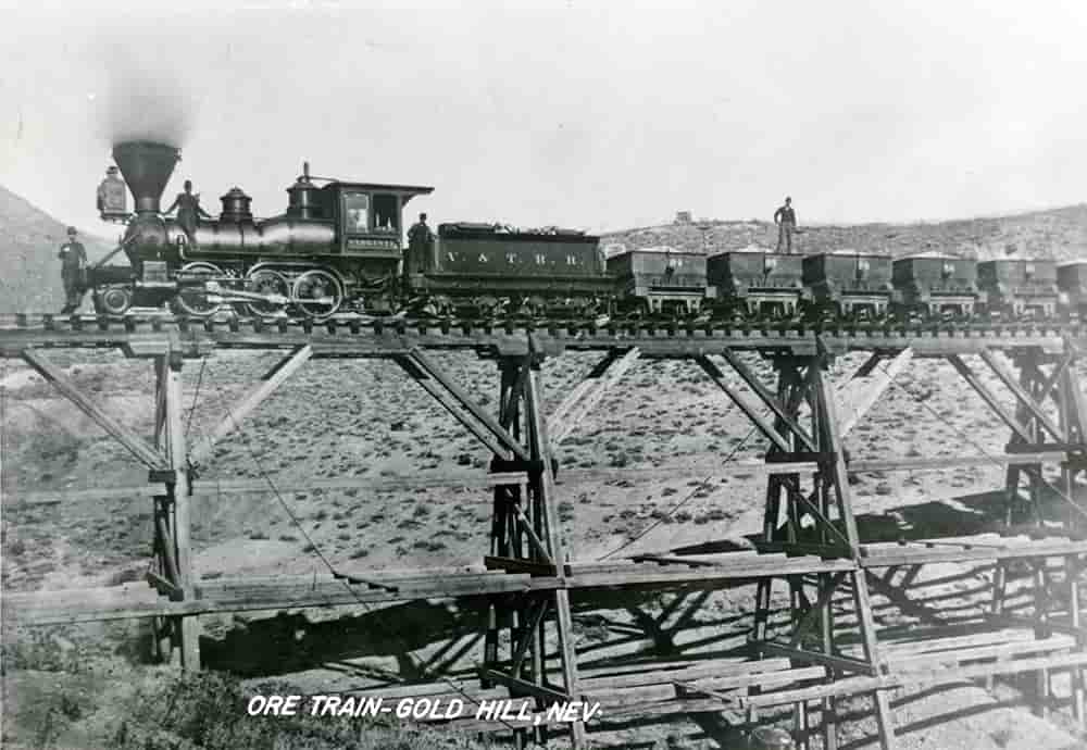 Black and white photograph of engine #4 of the V & T transporting cars full of ore across a train trestle.